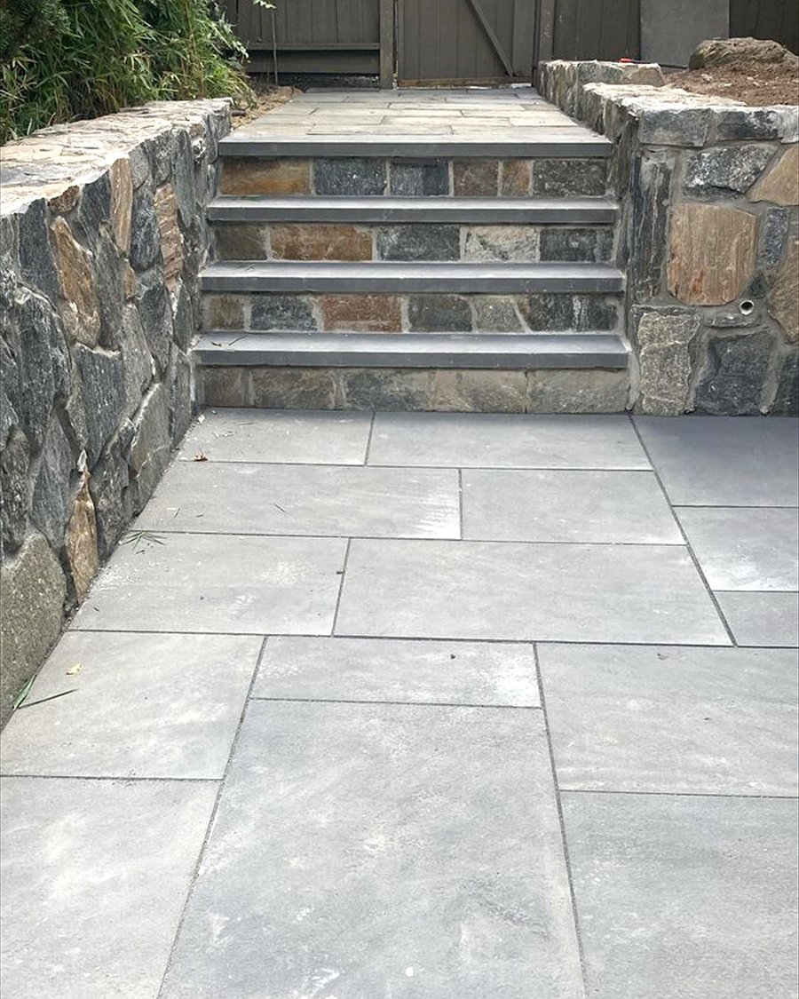 Stone faced steps with cut treads rising between two fieldstone walls onto a large format stone patio