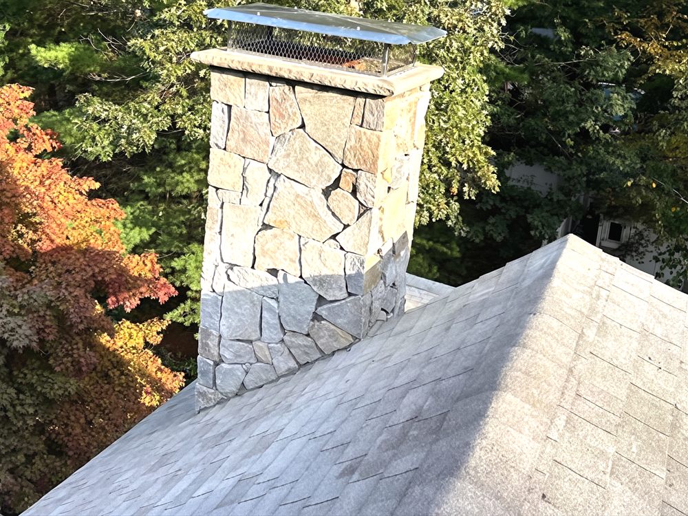 Stone faced chimney with a cap rising through a shingled roof