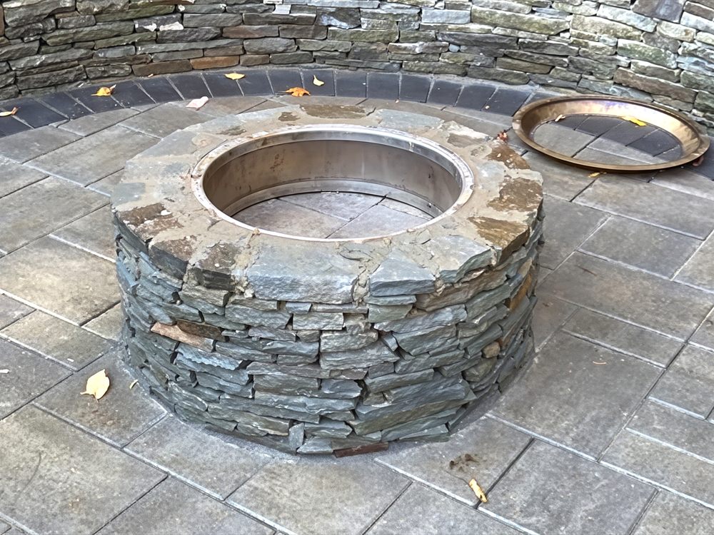 Round stone fire pit with a live fire set into a paver patio with a curved seat wall