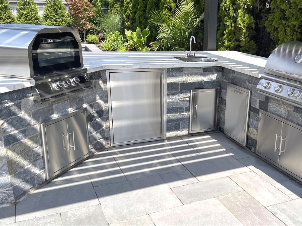Outdoor kitchen with stainless grill, sink and stone counter on a stone terrace
