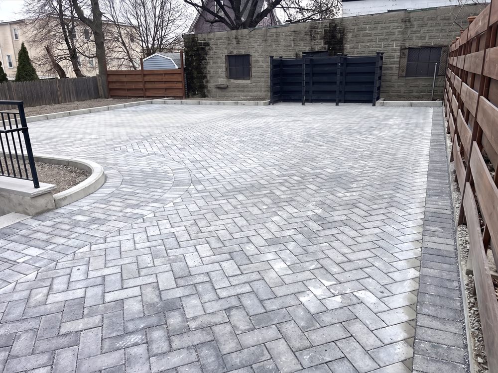 Large herringbone paver courtyard enclosed by a fence and a block wall